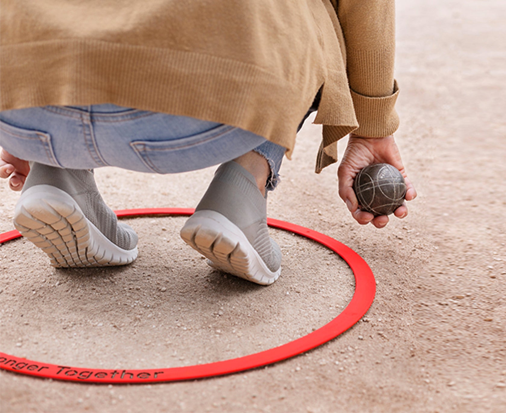 Gros plan sur un joueur de pétanque accroupi à l’intérieur d’un cercle en inox laqué rouge, tenant une boule prête à être lancée. Le cercle, posé sur le terrain, est gravé avec un message personnalisé.