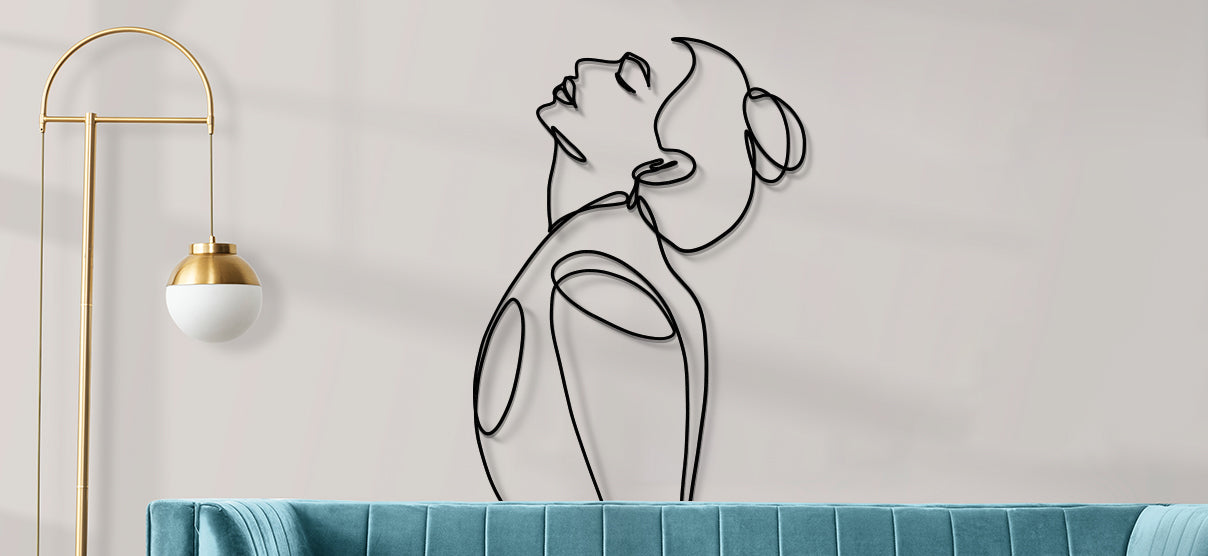 Un art mural en line art représentant une femme, accroché au-dessus d'un élégant canapé bleu. À côté, un lampadaire design diffuse une lumière douce, créant une atmosphère chaleureuse et moderne dans l’espace.